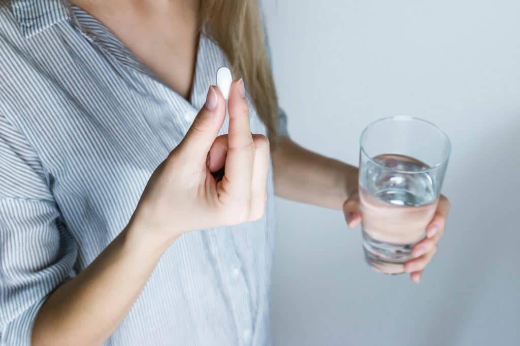 Vrouw neemt pijnstilling met water na implantaatbehandeling en vraagt zich af hoelang pijn na plaatsen implantaat duurt.